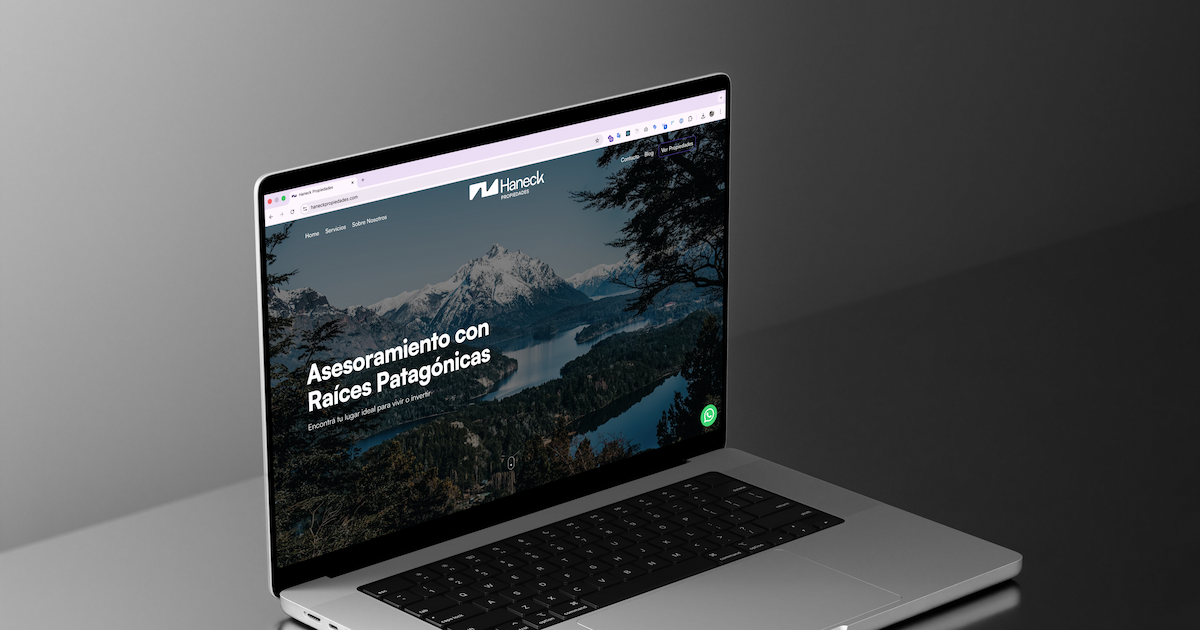Sitio web de Haneck Propiedades abierto en una notebook: portada con foto de la Patagonia y botón de WhatsApp